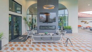 Ein Sitzbereich im Freien mit modernem Design, inklusive einer Couch und Sesseln, einem flachbildschirmfernseher an einer strukturierten Wand und einem gemusterten Boden.