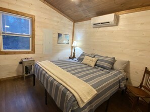 Ein gemütliches Schlafzimmer mit Bett, Nachttisch, Lampe und einem Fenster.