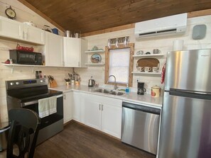 A compact kitchen with white cabinets, a stainless steel refrigerator, a microwave, an oven, and a sink.