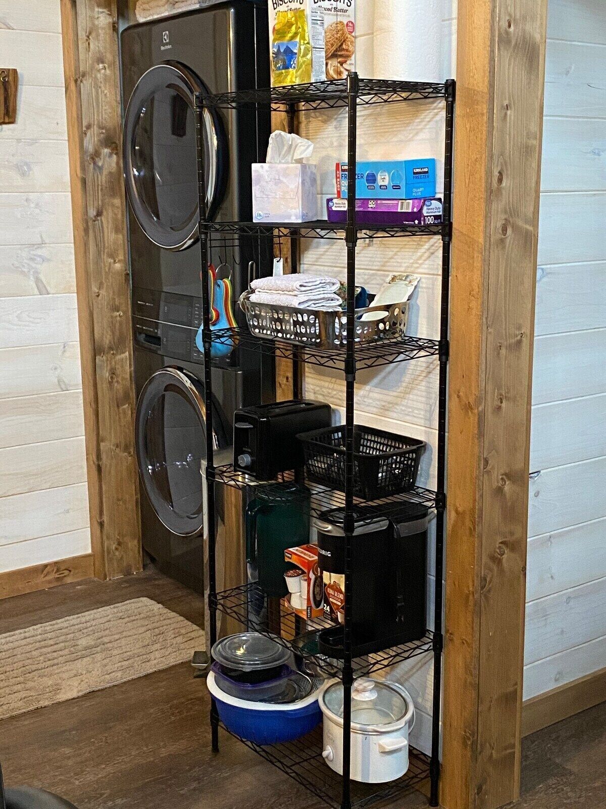 A kitchen area with a built-in washer and dryer, shelves with kitchenware, and a small refrigerator.