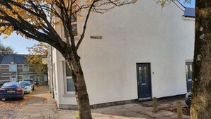 Un bâtiment blanc avec une porte noire, une plaque indiquant le nom de la rue, et des voitures garées le long du trottoir.