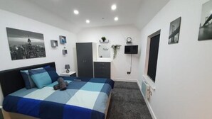 Une chambre à coucher avec un lit, une armoire, un bureau, une télévision et une fenêtre.