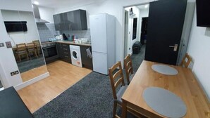 Une cuisine de taille réduite, équipée d’un lave-linge, d’une table à manger avec des chaises et d’une porte sombre.