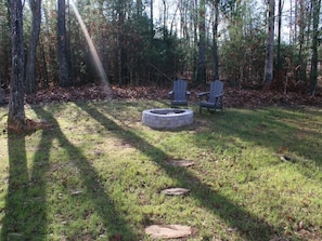 A forested area with a circular stone fire pit and two Adirondack chairs. - Blue Rock Escape by Buffalo Mtn Getaway (Floyd)