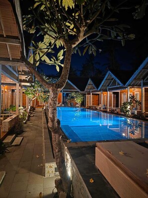 A pool area with a tree, lounge chairs, and wooden buildings. - Nusa Summerville (Gili Trawangan)