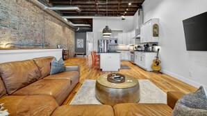 A modern living room with a leather sofa, a round coffee table, and a brick wall. - Luxury Loft DWTN | Whiskey Trail + River + Lake (Fayetteville)