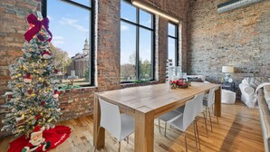 A modern kitchen with a brick wall, large windows, and a wooden dining table. - Luxury Loft DWTN | Whiskey Trail + River + Lake (Fayetteville)