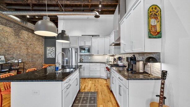 A modern kitchen with white cabinets, a black countertop, and a wooden floor. - Luxury Loft DWTN | Whiskey Trail + River + Lake (Fayetteville)
