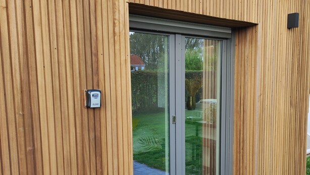 A modern building with a wooden facade, a glass door entrance, and a tiled roof. - Cosy country B&B  (Comines-Warneton)