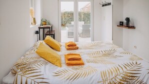 A bedroom with a bed, a small table with a plant, and a view of the outside through a sliding door. - Cosy country B&B  (Comines-Warneton)