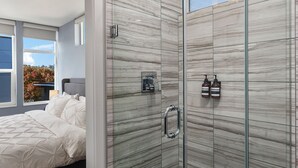 Ein modernes Badezimmer mit einer gläsernen Dusche, Marmorwänden und einem Bett mit weißer Bettwäsche.