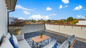 Eine Dachterrasse mit einer Couch, einem kleinen Tisch und Topfpflanzen.