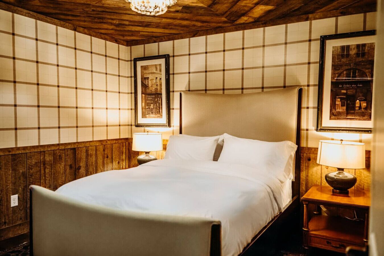 Cama bem arrumada com lençóis brancos, duas luminárias de cabeceira e um quadro na parede.