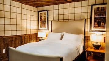 Cama bem arrumada com lençóis brancos, duas luminárias de cabeceira e um quadro na parede.