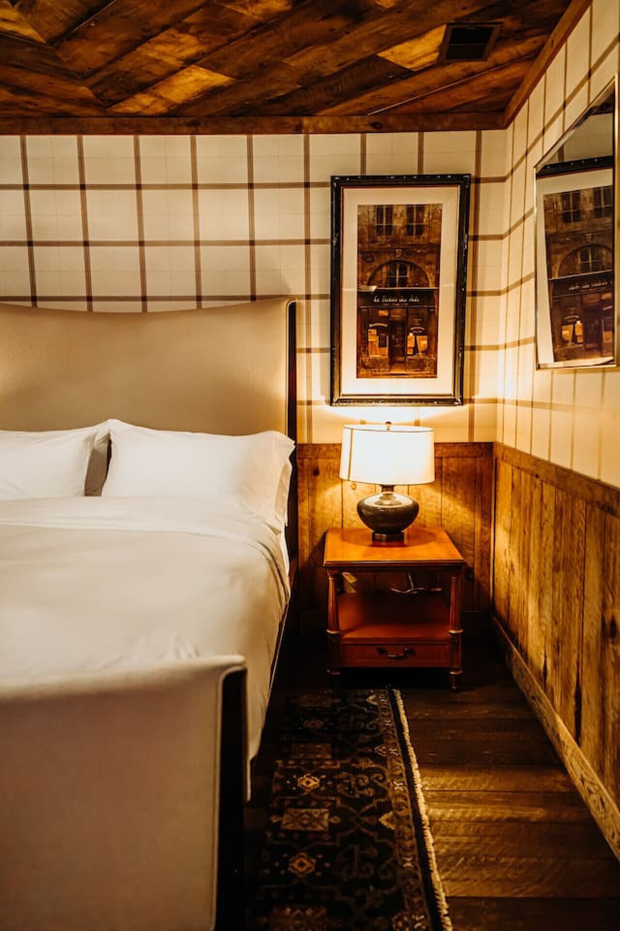 Hotellihuone, jossa on sänky, yöpöytä lampun kanssa ja seinällä oleva kehystetty kuva.