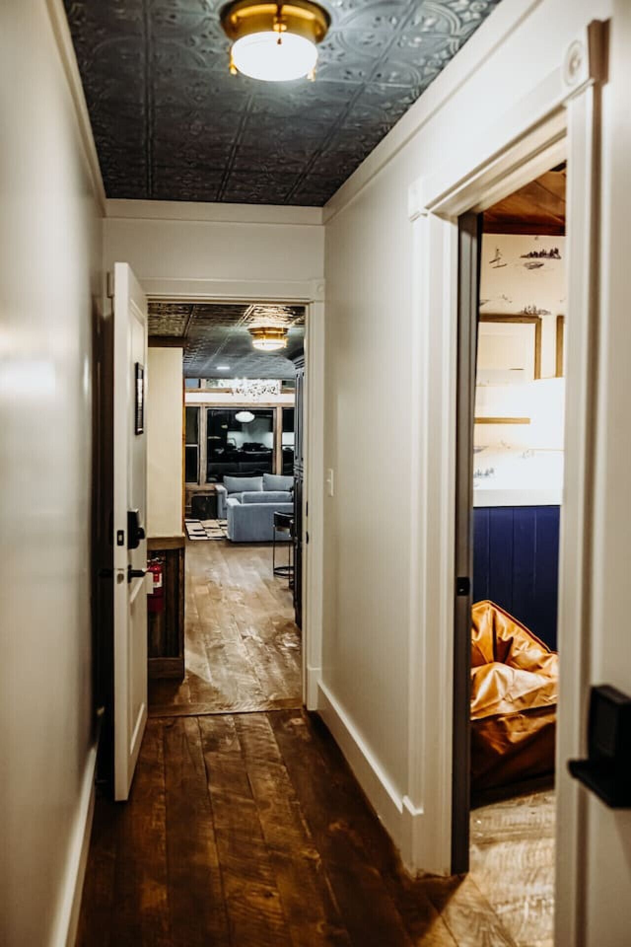 Un couloir étroit, doté d’un plancher en bois, mène à une pièce où se trouvent un lit et un mur bleu.