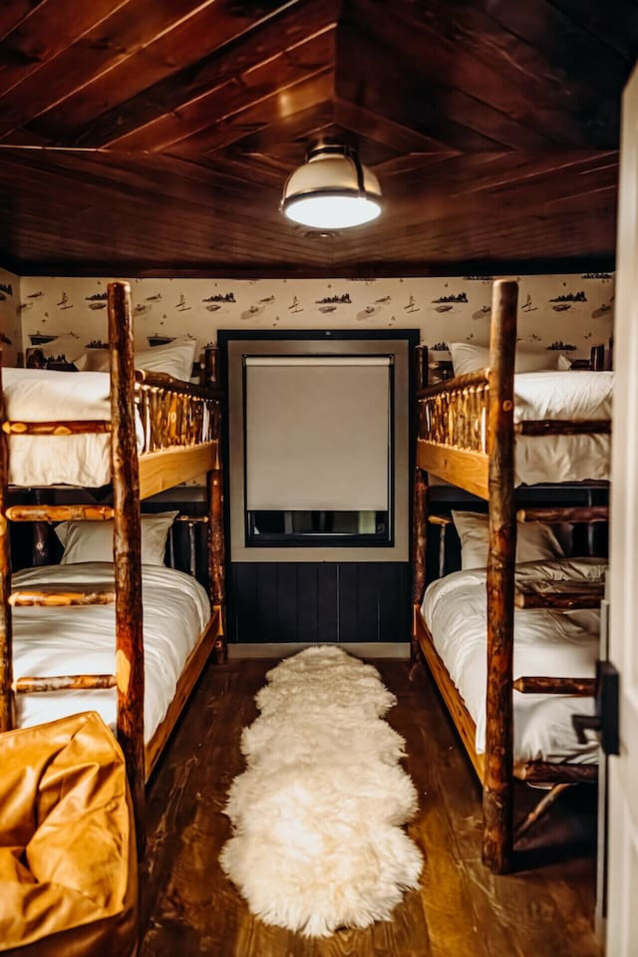 Une pièce avec des lits superposés, un tapis en fourrure, des murs en bois et un luminaire au plafond.