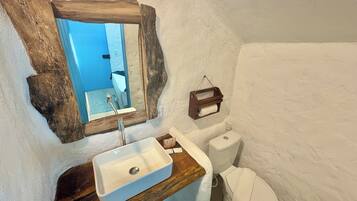 A bathroom with a wooden vanity, a white sink, a mirror, and a toilet.