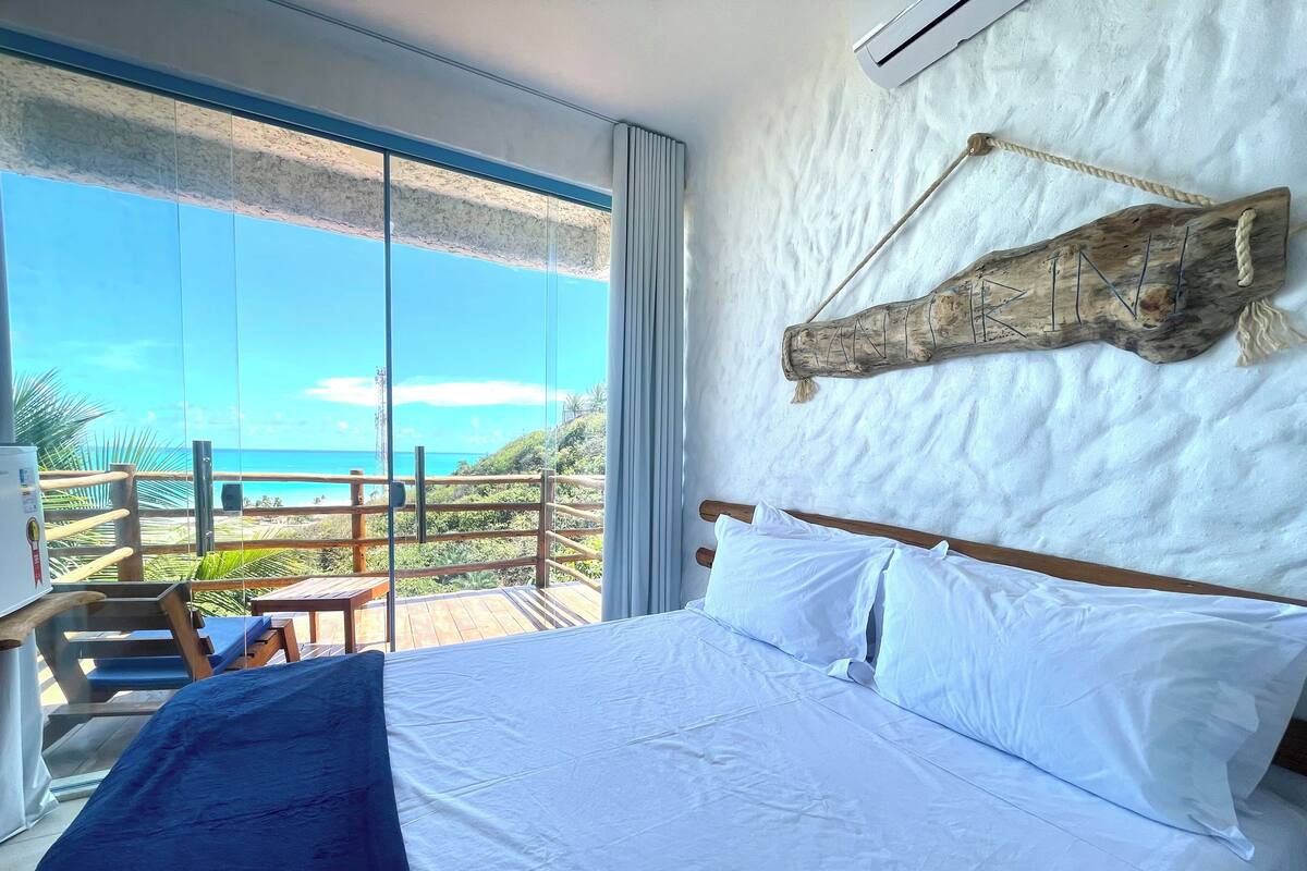A bedroom with a large bed, a view of the beach, and a wooden headboard.