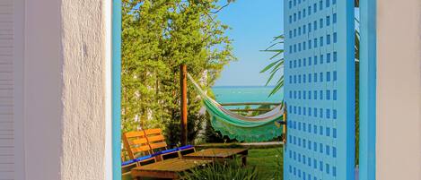 An open doorway leading to a hammock and a wooden bench by a pool, with a clear view of the ocean.