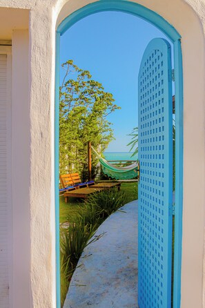 An open doorway leading to a hammock and a wooden bench by a pool, with a clear view of the ocean. - Casa Edom - Max Rev (Maceió)