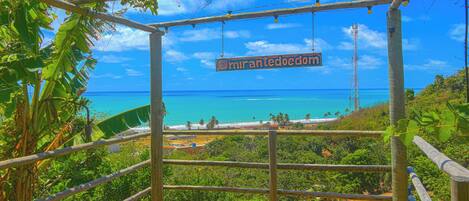 A wooden viewing platform with a sign reading "miranteedom" overlooking a beach and ocean.
