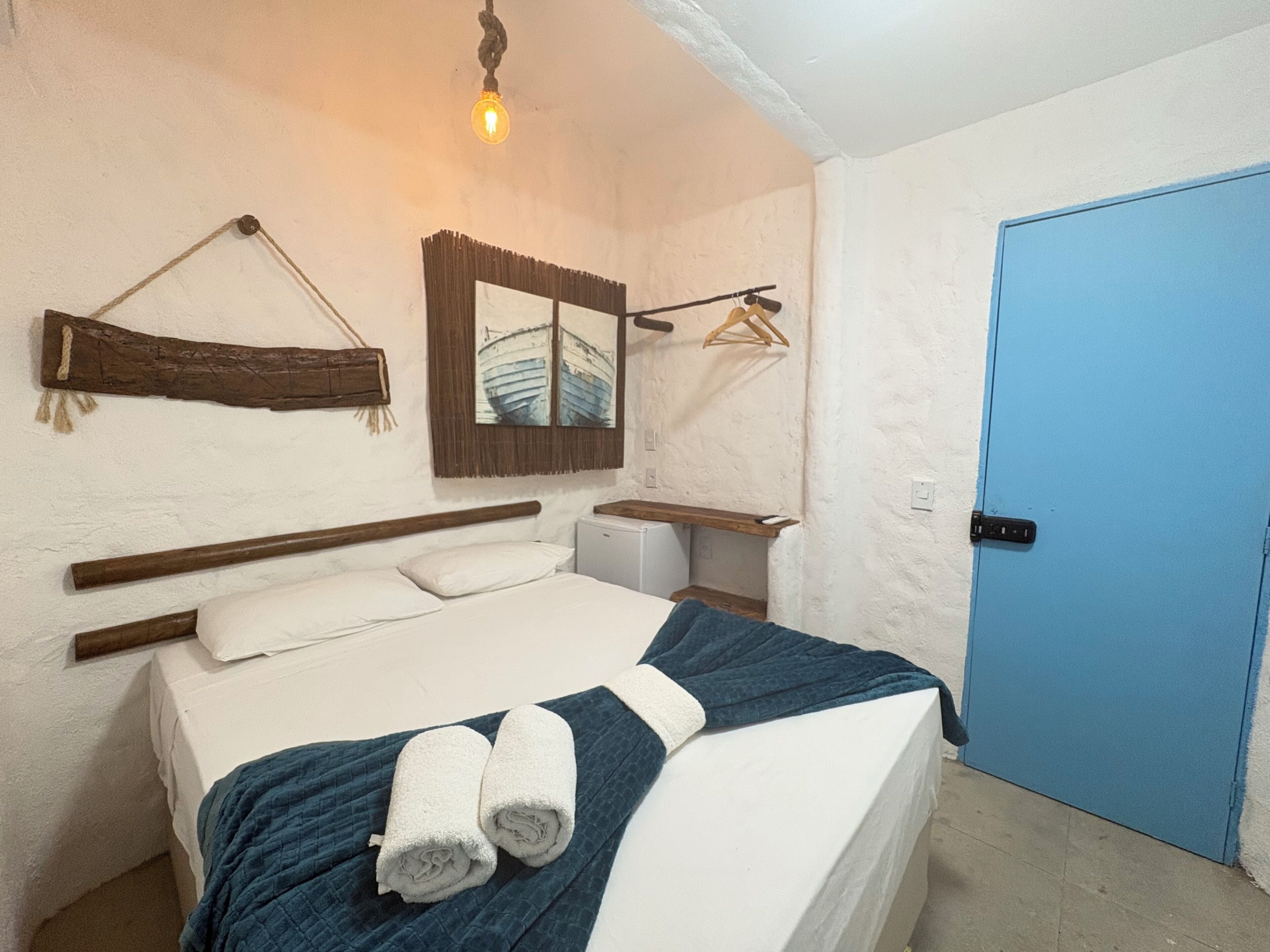 A bedroom with a bed, a bedside table, a mirror, a hanging light fixture, and a blue door.