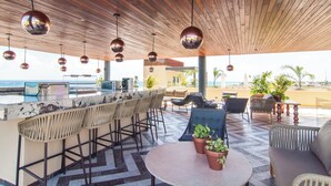 Eine Bar mit Holzboden, hängenden Kugelleuchten, einer Marmorplatte und Barhocker.
