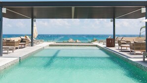 Ein Pool mit Meerblick, umgeben von Liegestühlen und einer schattigen Liegefläche.