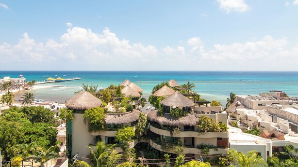 Ein Resort mit mehreren Gebäuden, darunter einige mit Strohdächern, mit Blick auf einen Strand und den Ozean.