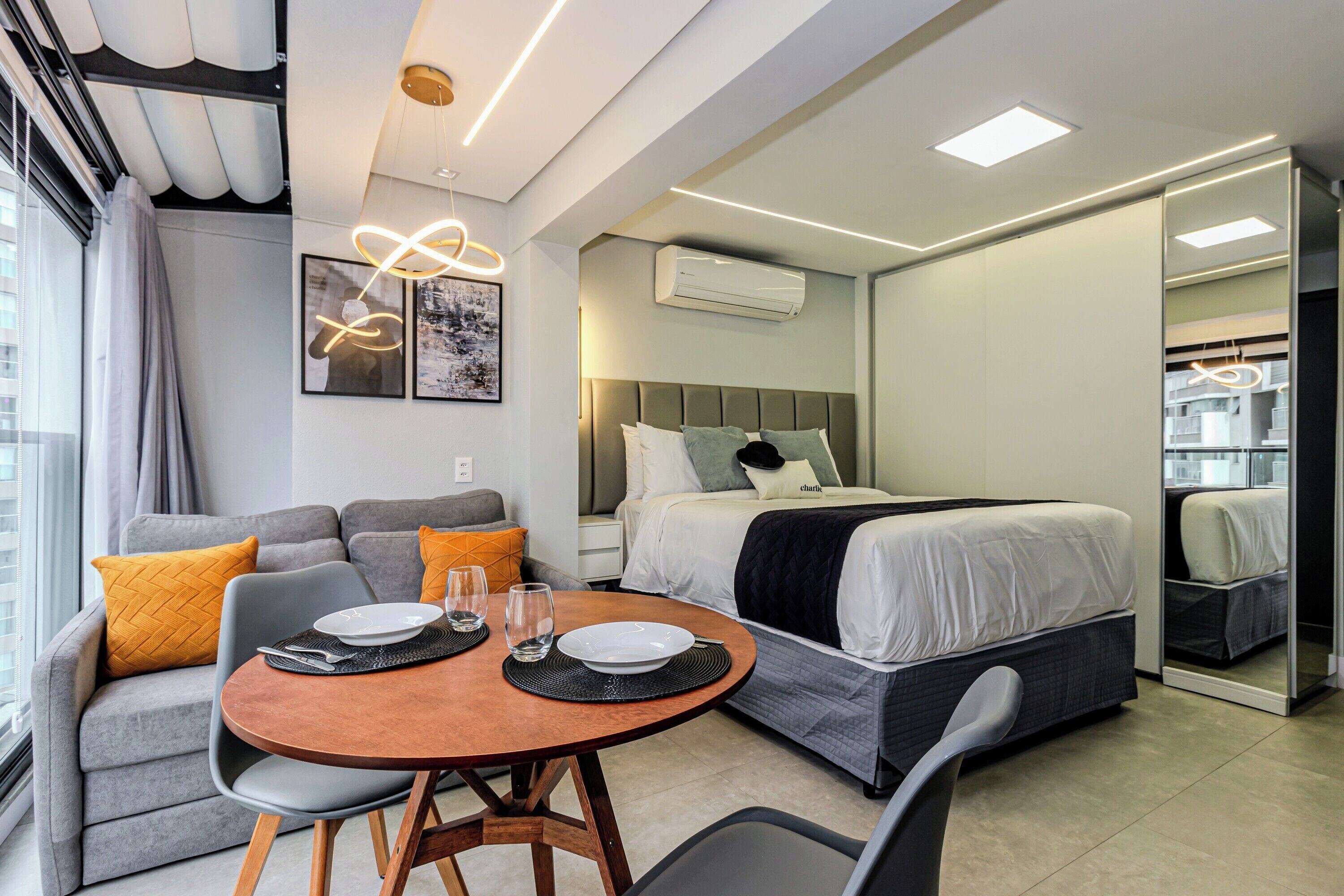 Quarto de hotel moderno com cama, sofá, mesa de jantar e espelho.