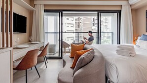 Habitació d'hotel moderna amb un llit gran, una taula de treball amb televisió de pantalla plana i un balcó amb vista a la ciutat.