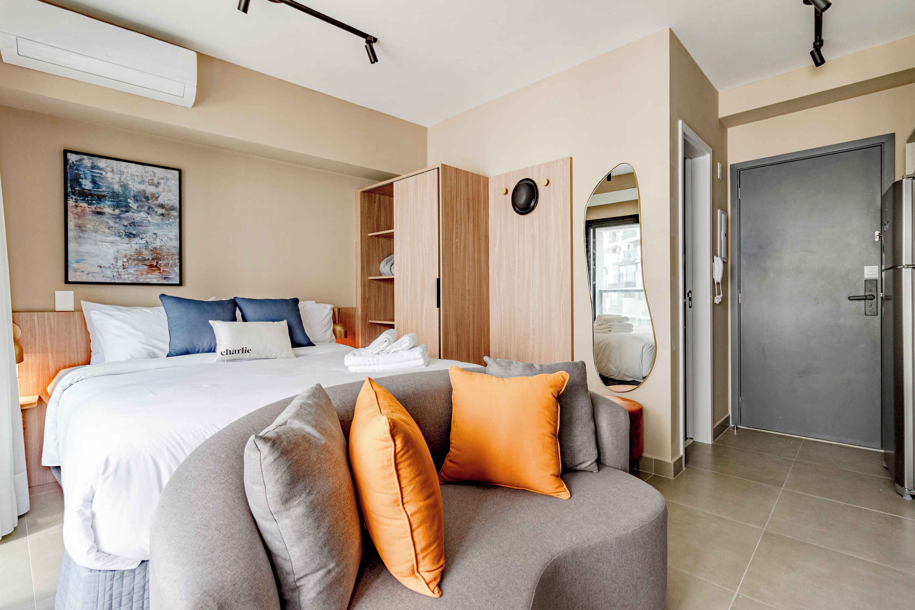 A modern hotel room with a large bed, grey sofa, and a wardrobe.