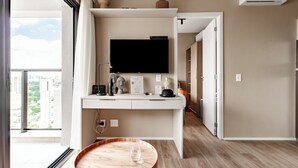 Habitació d'hotel moderna amb una finestra gran, un televisor de pantalla plana fixat a la paret, una taula rodona de fusta i un escriptori blanc amb una màquina de cafè.