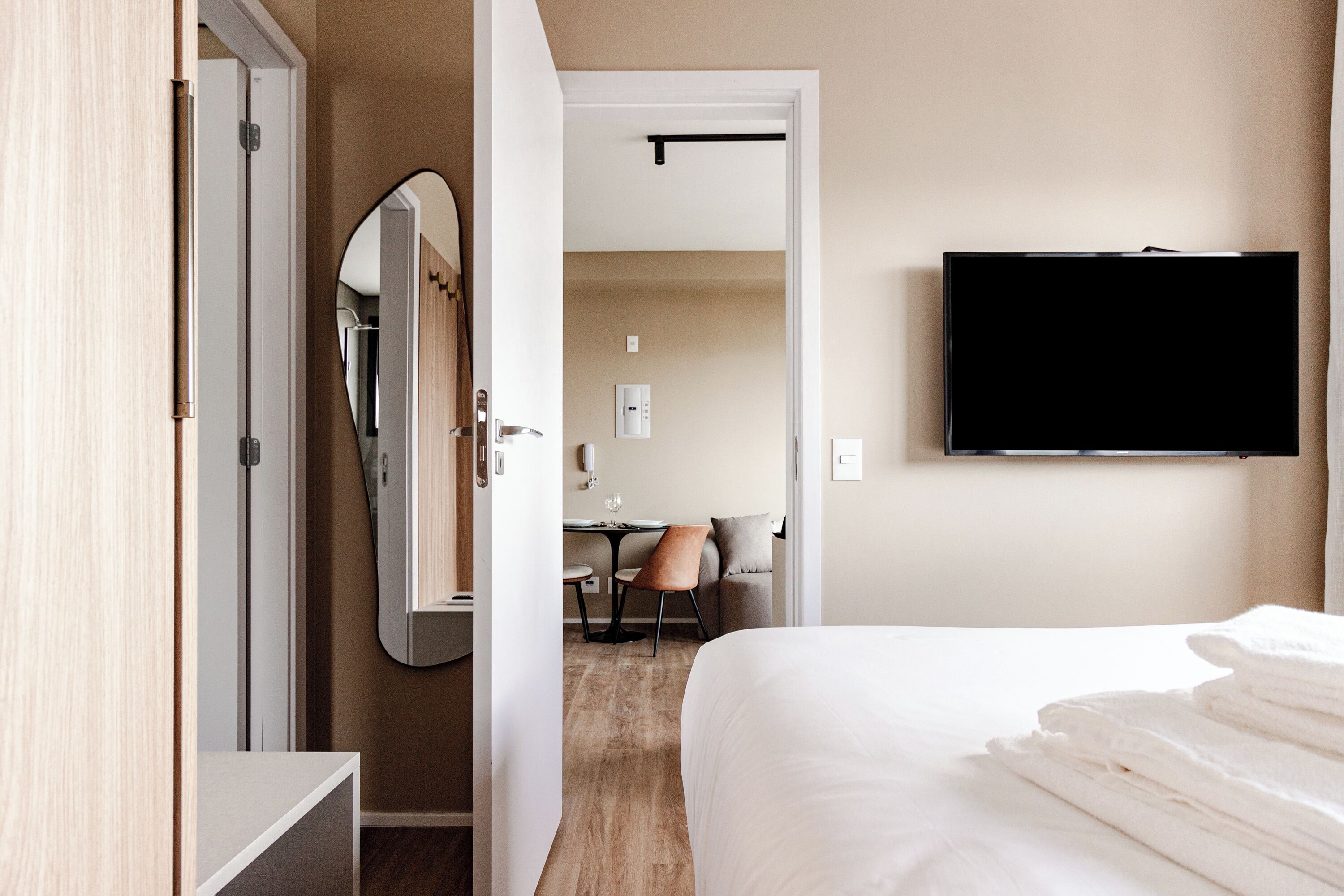 A hotel room with a bed, a TV mounted on the wall, a mirror, and a desk with a chair.