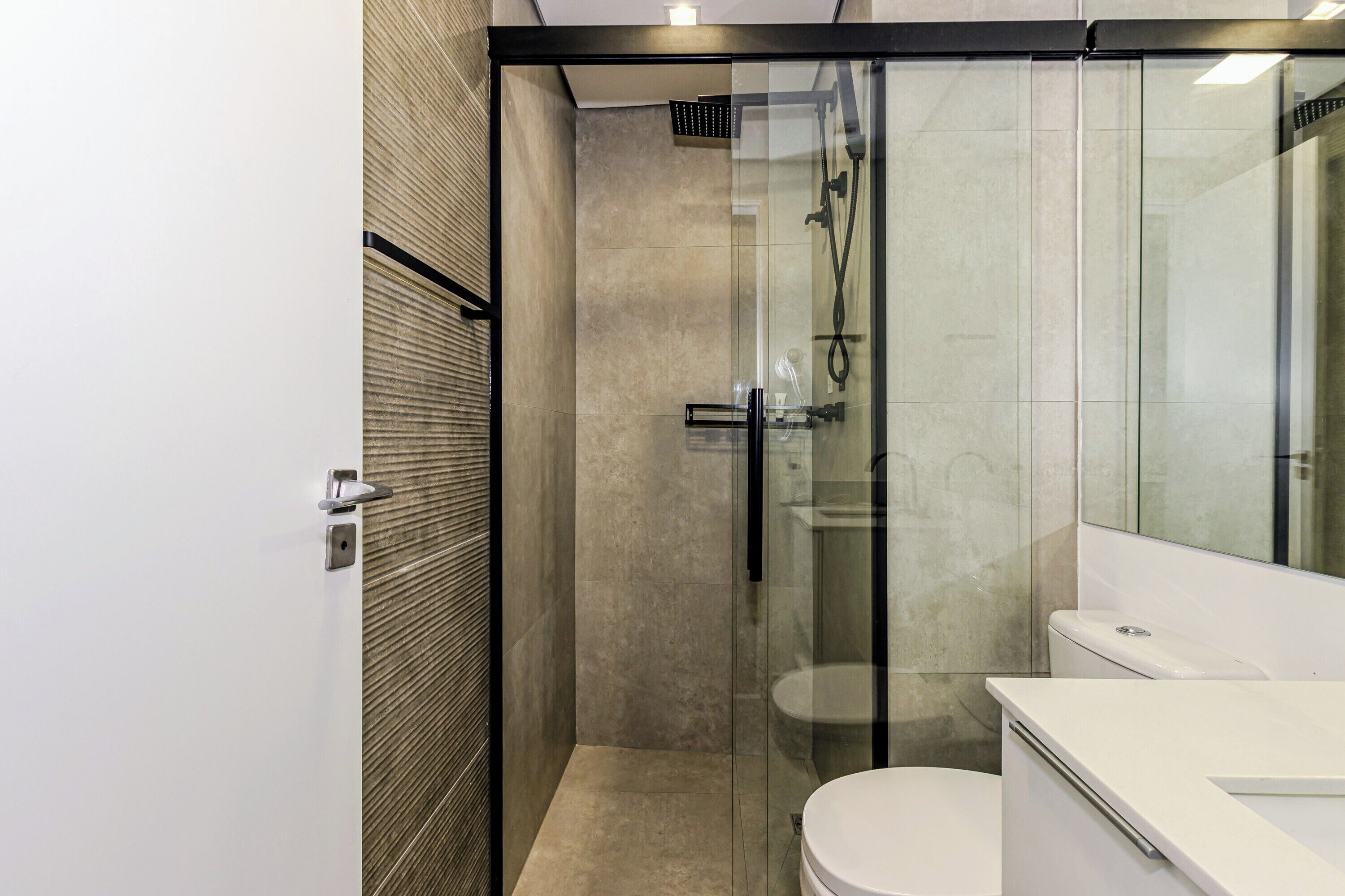 Une salle de bain moderne avec une douche à parois de verre, des toilettes blanches et un grand miroir.
