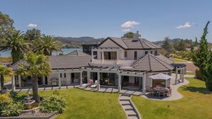 A large, modern house with a covered patio, a swimming pool, and a view of the water.