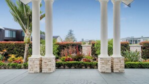 A covered outdoor area with white columns and stone bases, surrounded by landscaped gardens and modern buildings in the background.