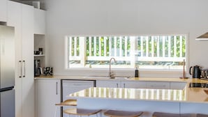 Eine moderne Küche mit weißen Schränken, einem großen Fenster und einer Bar mit Hockern.