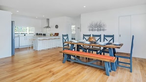 Eine moderne Küche mit weißen Schränken, einer zentralen Kochinsel und einem Essbereich mit Holztisch und blauen Stühlen.