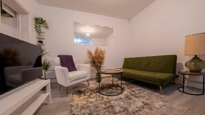 Ein modernes Wohnzimmer mit Flachbildfernseher, einem grünen Sofa, einem weißen Sessel und einem kleinen runden Tisch.