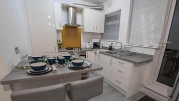 A compact kitchen with white cabinets, a stainless steel range hood, a sink, and a window with blinds.