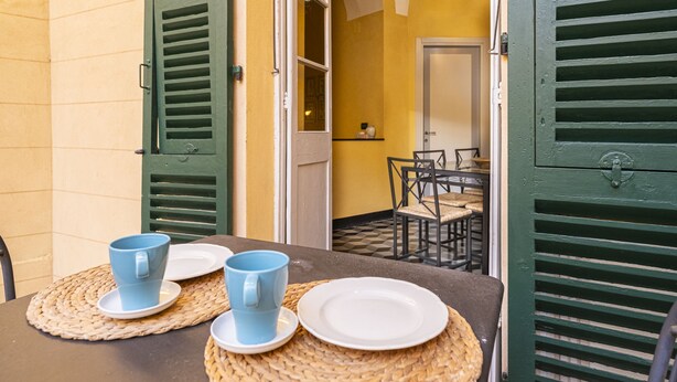 Un comedor con una mesa lista para dos personas, con individuales tejidos, una taza azul y un plato blanco.