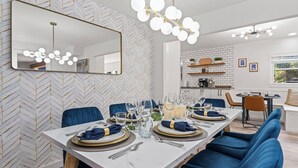 A modern dining area with a long table set for six, blue upholstered chairs, a large mirror, and a chandelier. - HotTub, FirePit, Pets, Pool Table, Outdoor Dining (Hendersonville)