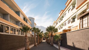 Un long couloir bordé de palmiers et de bâtiments dotés de balcons, qui mène vers une montagne.