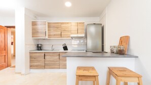 Une cuisine moderne avec des meubles en bois, un réfrigérateur en acier inoxydable et deux tabourets en bois.