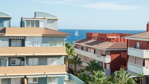 Un hôtel situé sur la côte, doté de nombreux balcons, offrant une vue sur la mer et bordé de palmiers.