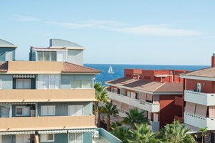 A coastal hotel with multiple balconies, a view of the sea, and palm trees.