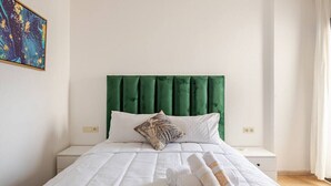 A neatly made bed with white bedding and a green upholstered headboard.