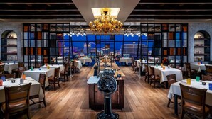 Un restaurante con barra central, mesas, sillas y vista a un paisaje urbano de noche.